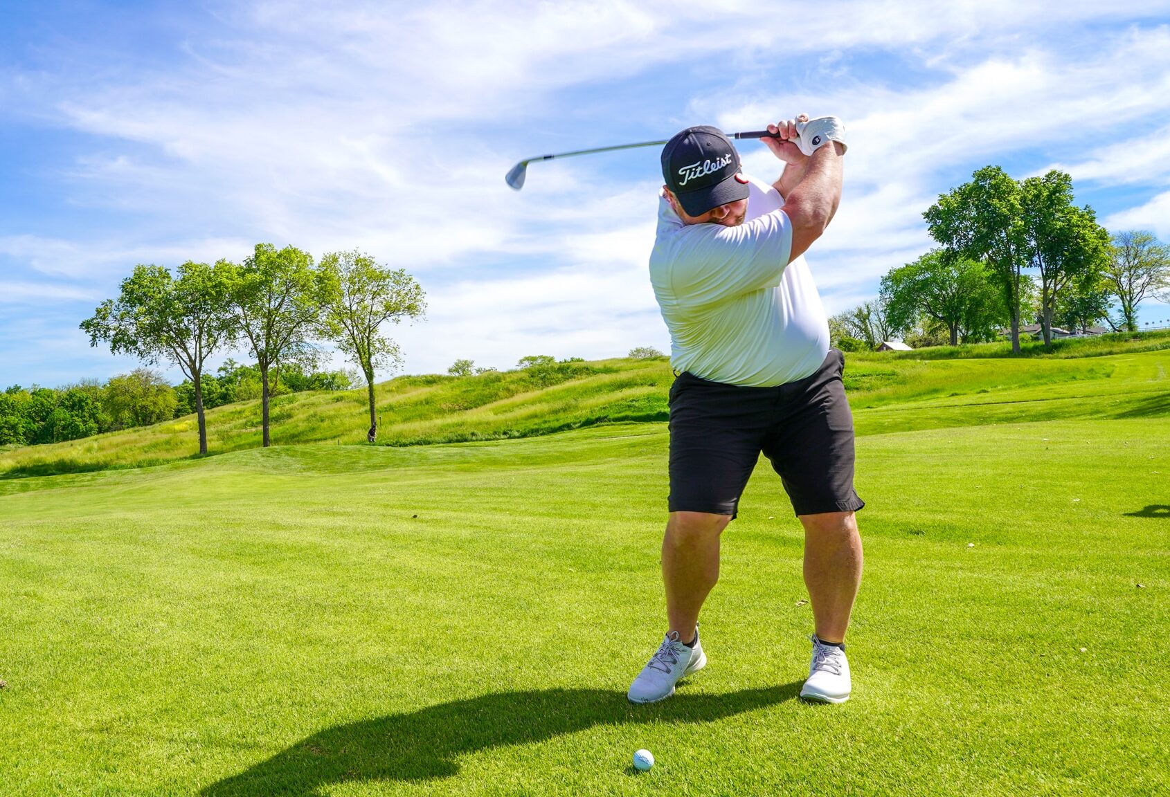 A golfer is in his backswing on the fairway as he prepares to hit the ball toward the green.