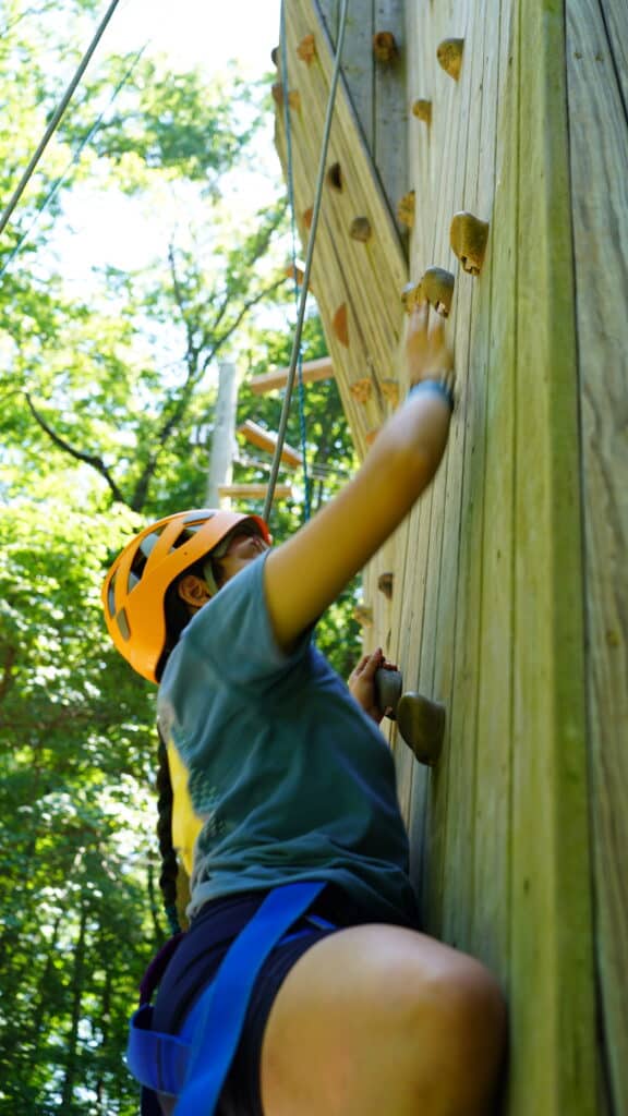 An Adventure Camp attendee is climbing the wall. 