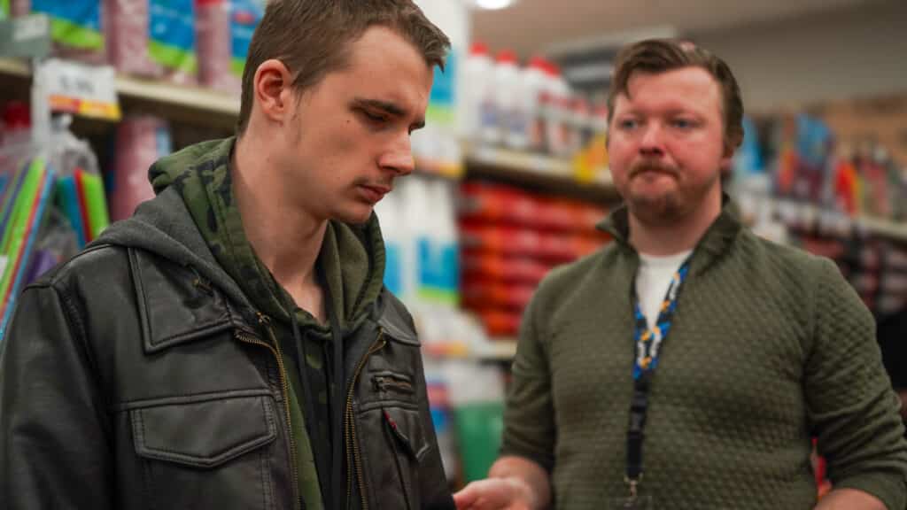 Baron, in the foreground, is at a grocery store working with Jason to learn shopping skills that will help him be more independent. 
