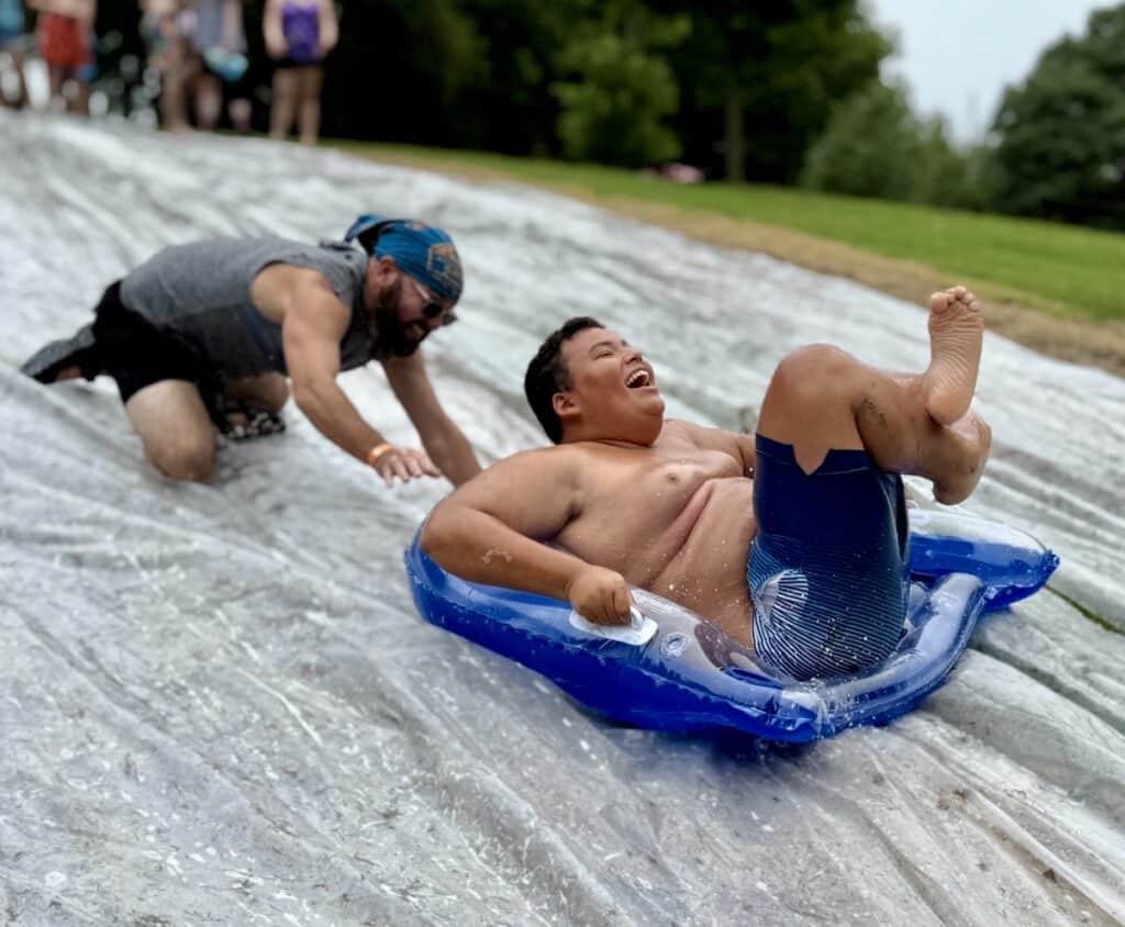 Jake is pushing Darius down the water slide at Adventure Camp.