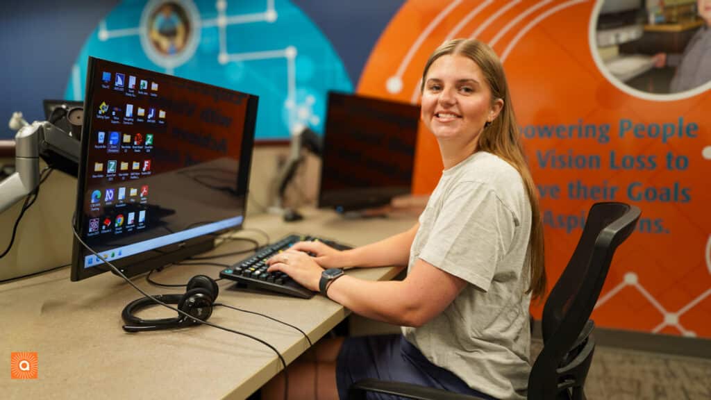 Riley is seated at a computer in the Alphapointe Computer Lab. She is turned toward the camera and is smiling. 