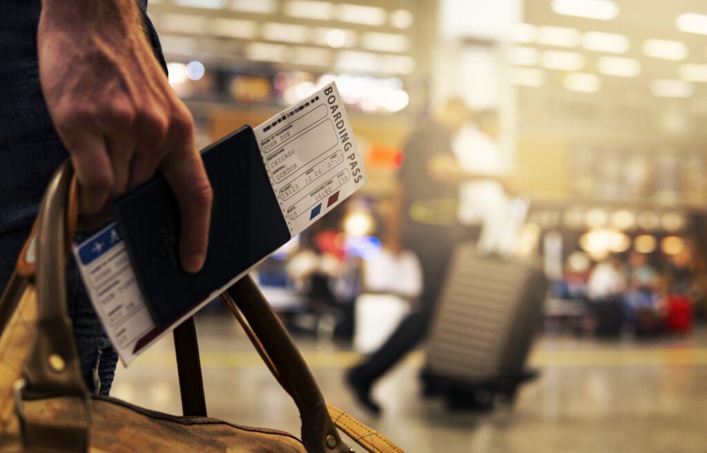 A person is holding a boarding pass with the airport in the background.