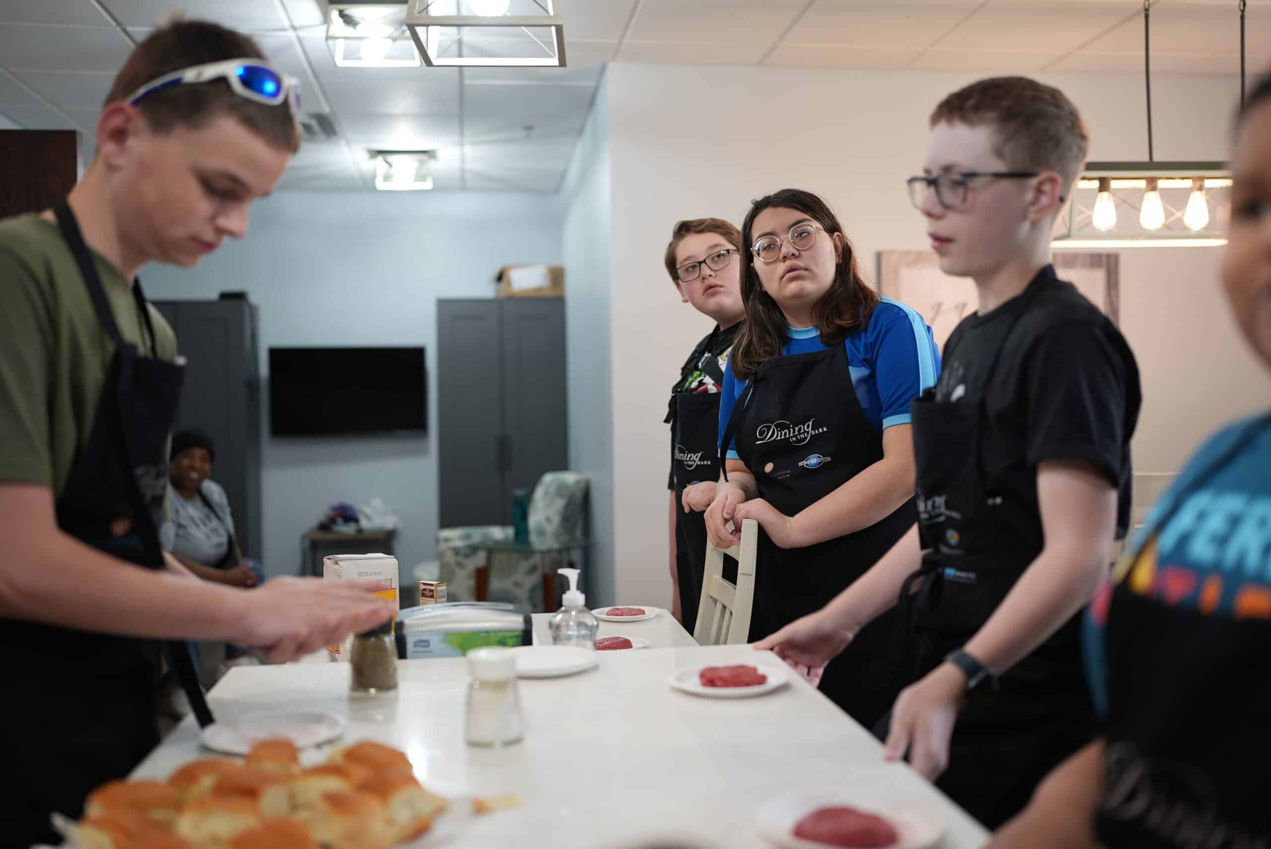 A group of Kids in the Kitchen attendees are at the island counter preparing food.