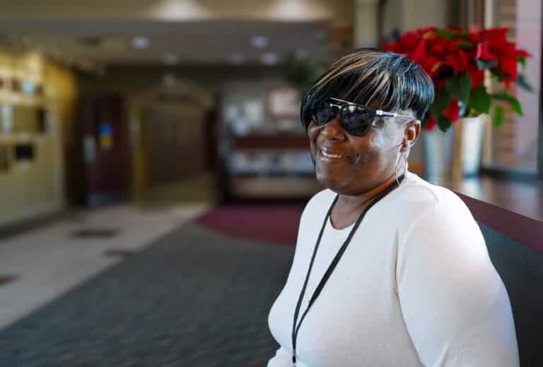 Miyya is seated in the lobby of the Alphapointe Life Skills Campus. She is smiling at the camera.