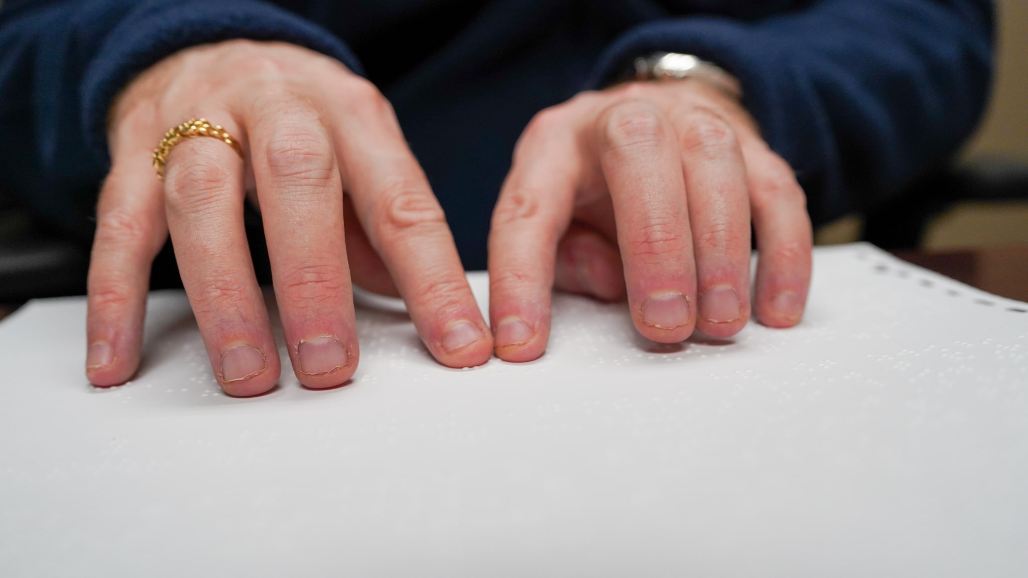 Cameron's hands are moving across a page filled with Braille.