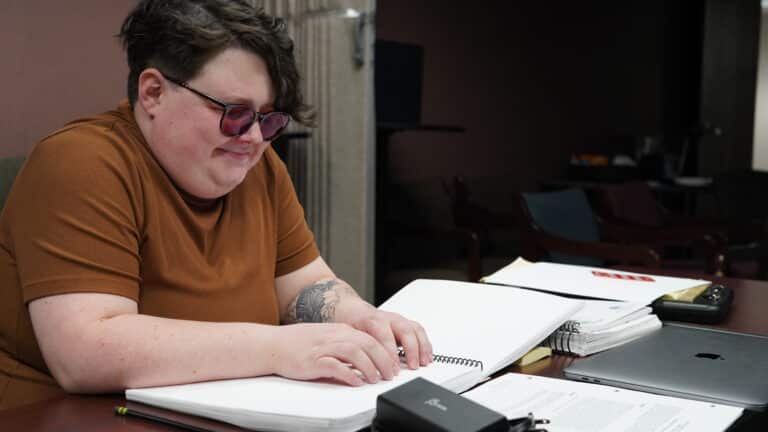 RJ is using both hands to run across a book of Braille