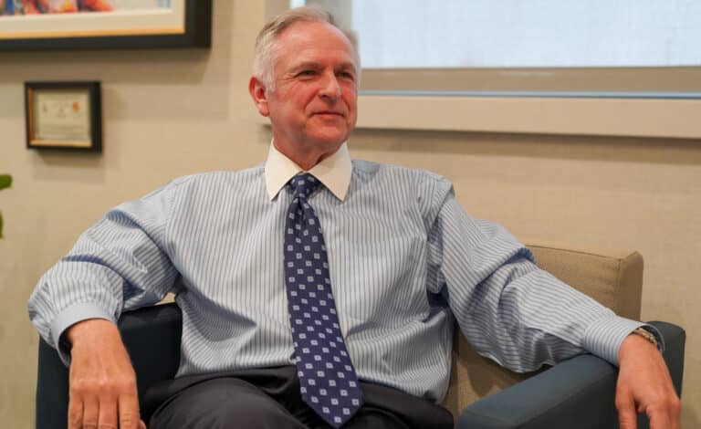 Alphapointe President and CEO, Reinhard Mabry, is seated and looking to the right of the camera as he smiles.