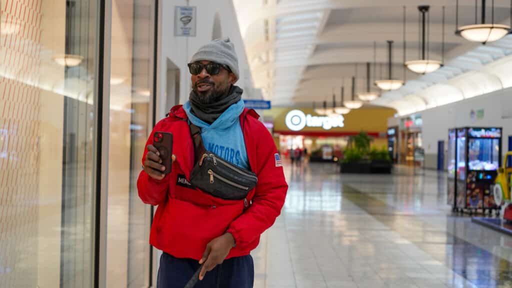In this photo, he is in the main atrium of the mall. He has his cane in one hand and his phone in the other.