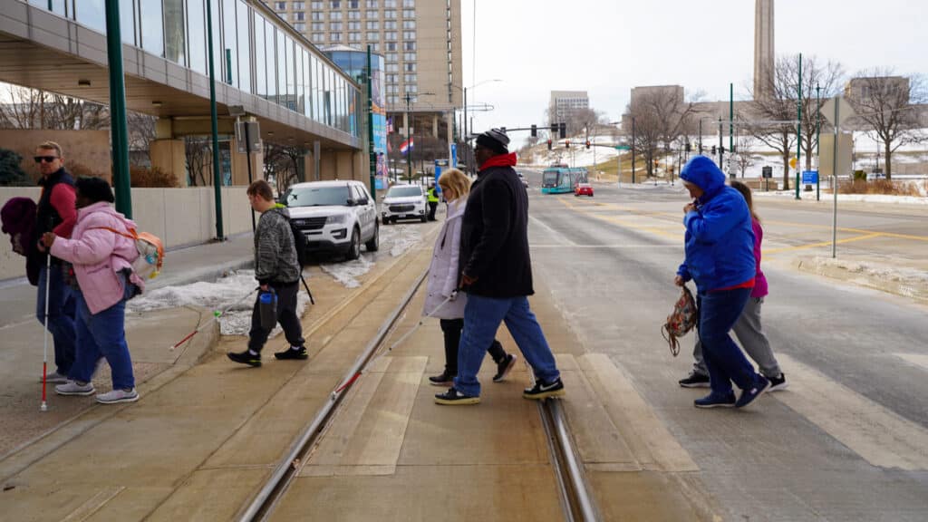 In this image, Alphapointe clients are using a crosswalk in downtown Kansas City. They are navigating to the trolley station so they can board and ride - all a part of the learning experience.