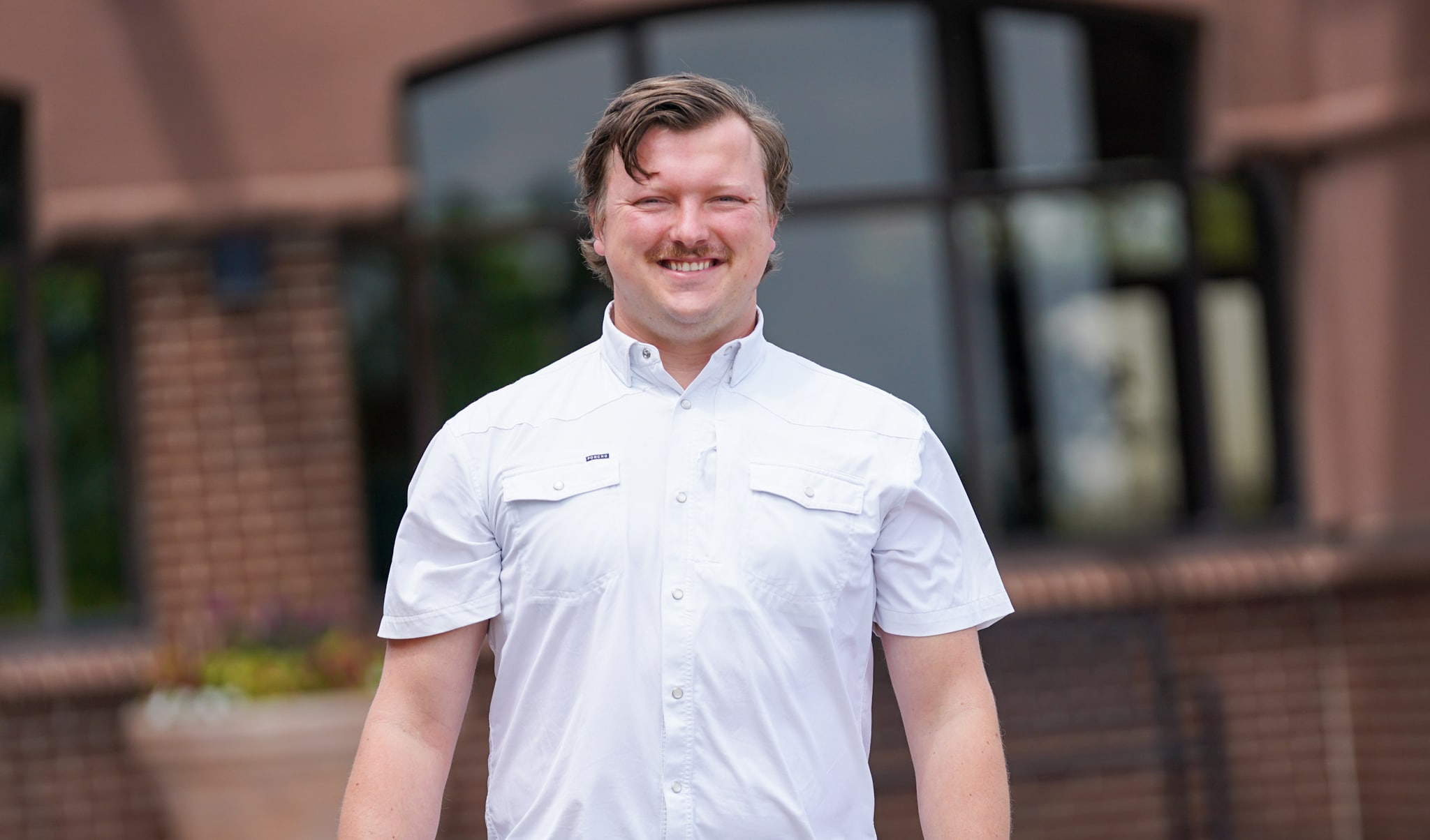 Jason is standing outside of the Alphapointe building and is smiling at the camera.