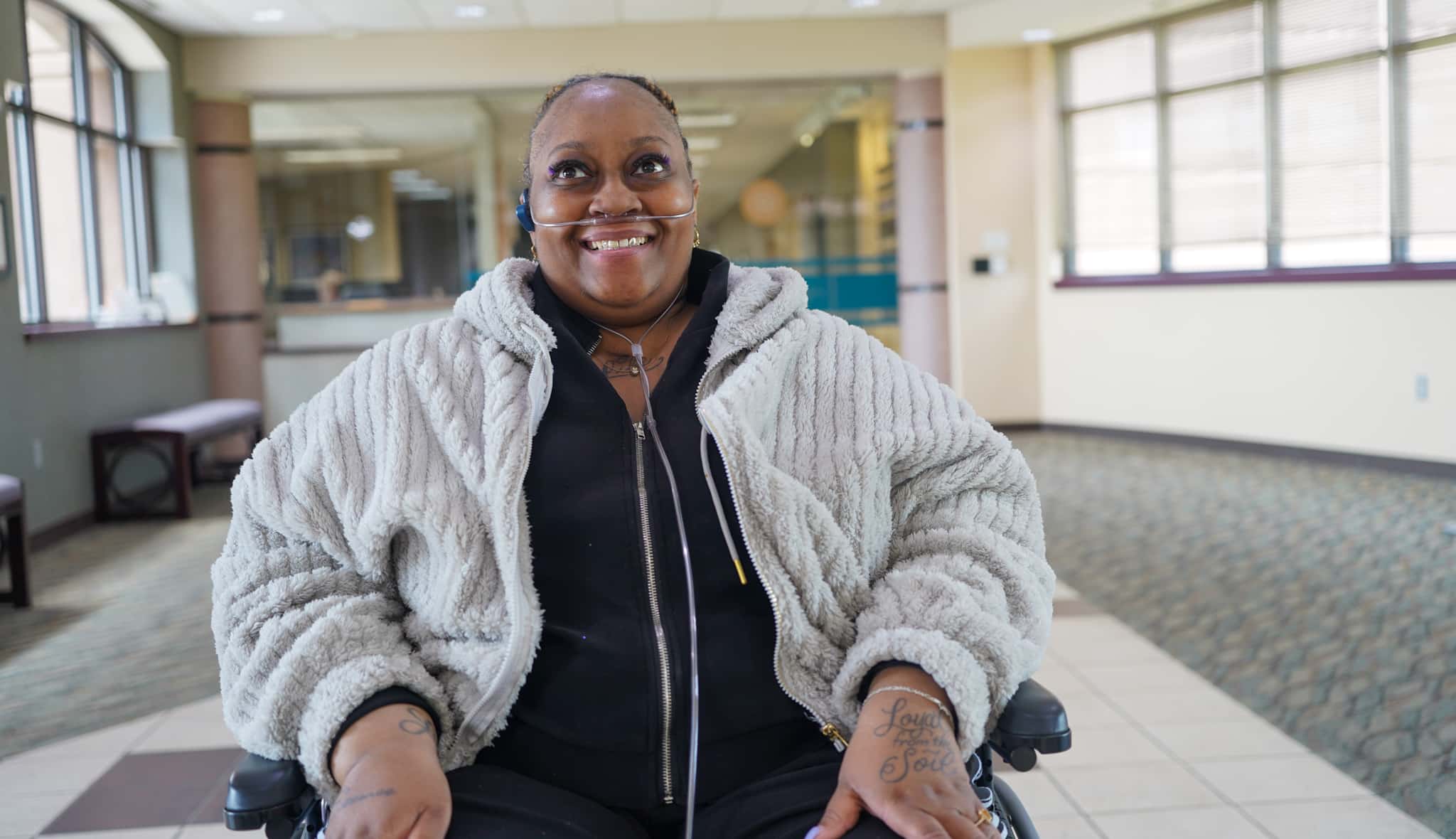Tara is seated in her chair and is smiling at the camera. She is in the Alphapointe lobby.