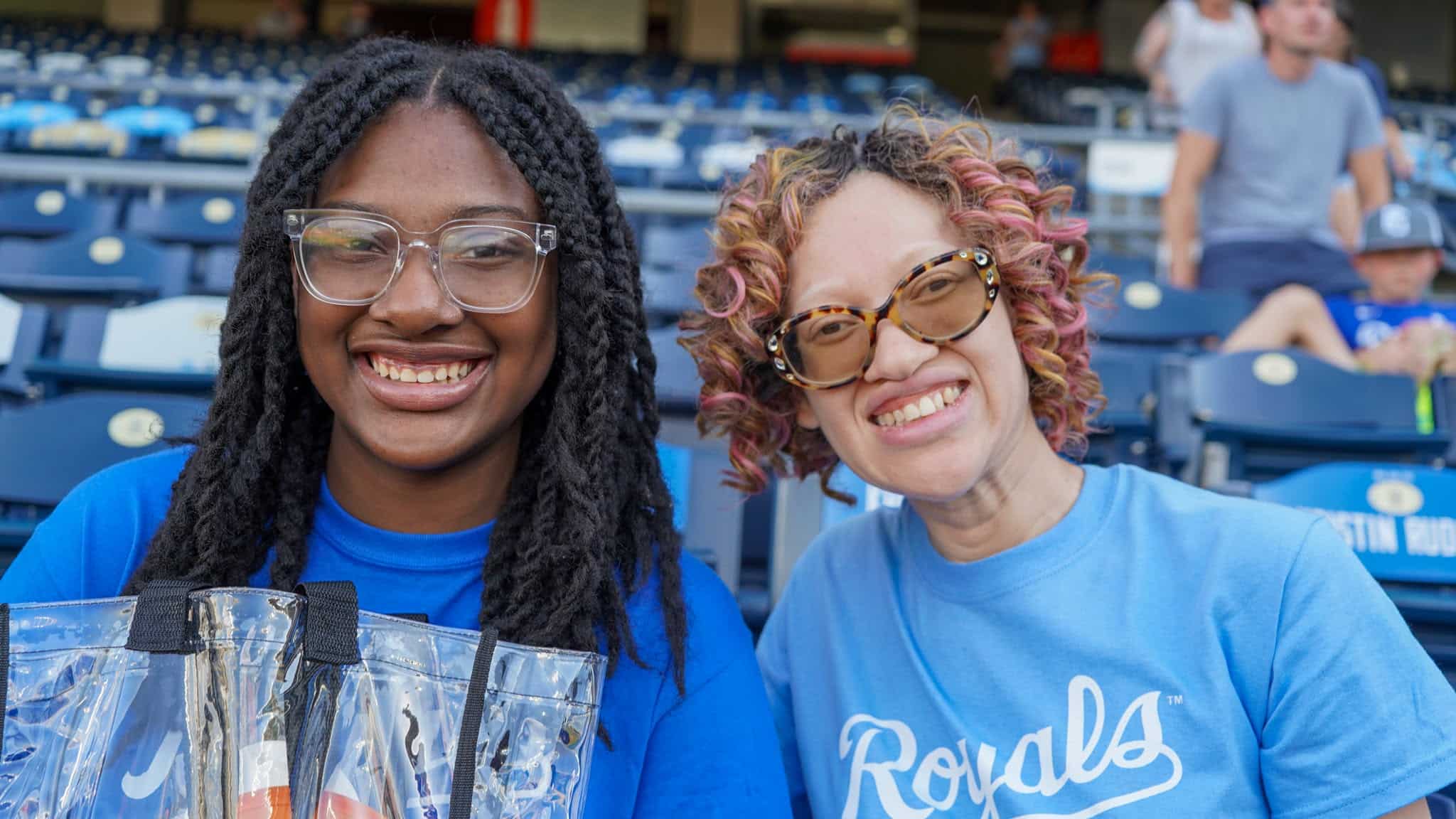 Two attendees are seated at the stadium and are smiling at the camera.