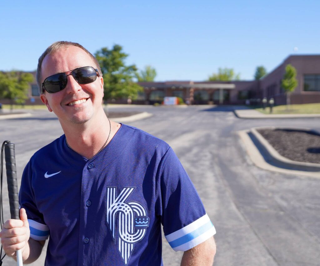 Cameron is pictured in front of the Alphapointe building. He is smiling and holding his cane.