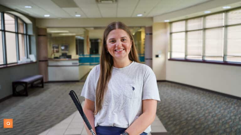 Riley is standing in the Alphapointe lobby and is smiling at the camera.